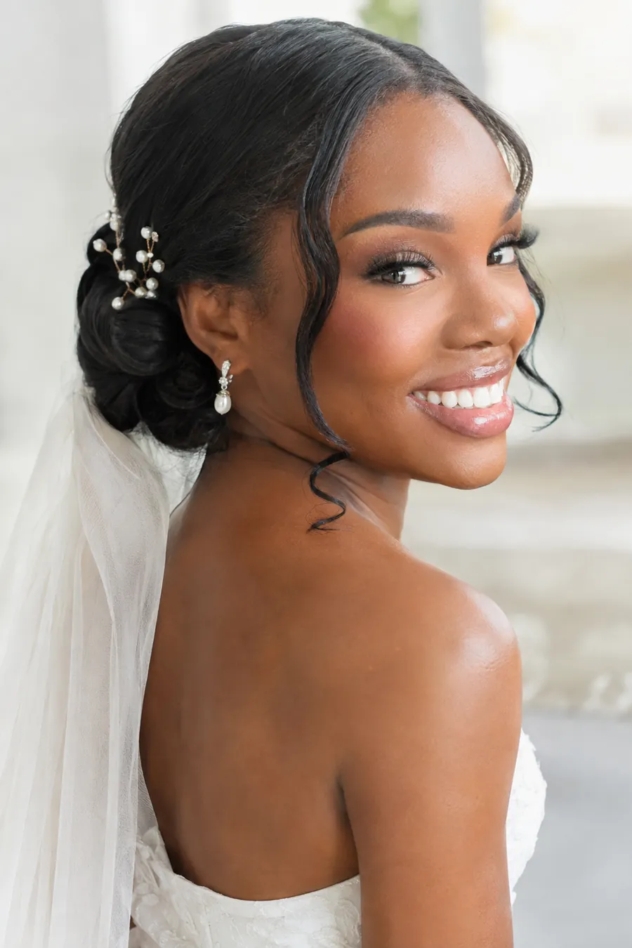 Joyful bride with a low bun accented with pearl hairpins and a veil